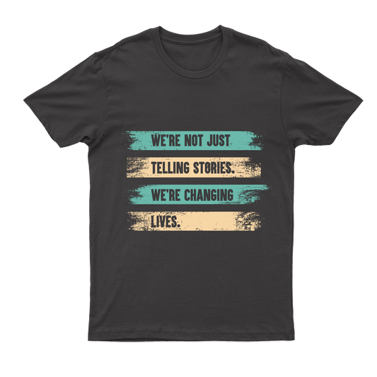 A gray T-shirt with a printed message on 4 lines, each line on an alternating painted stripe background of teal and tan: "We're not just telling stories, we're changing lives."