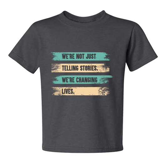 A gray youth T-shirt with a printed message on alternating stripes of teal and tan painted background: "We're not just telling stories, we're changing lives."