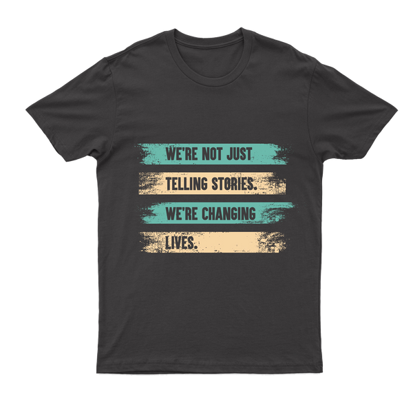 A gray T-shirt with a printed message on 4 lines, each line on an alternating painted stripe background of teal and tan: "We're not just telling stories, we're changing lives."