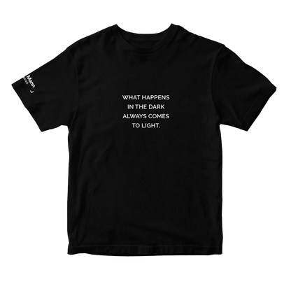 Black short sleeve t-shirt with the text "WHAT HAPPENS IN THE DARK ALWAYS COMES TO LIGHT." printed in white. It also features a printed tag on the right sleeve: the 'Dhar Mann Studios' logo. 